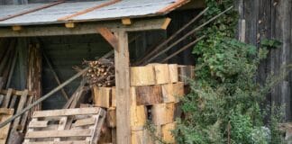 Jak bezpiecznie składować drewno kominkowe w ogrodzie w Piasecznie, Warszawie i okolicach Stos drewna kominkowego przy drewnianym składziku w ogrodzie
