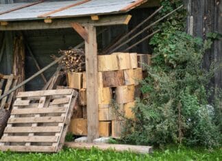 Jak bezpiecznie składować drewno kominkowe w ogrodzie w Piasecznie, Warszawie i okolicach Stos drewna kominkowego przy drewnianym składziku w ogrodzie
